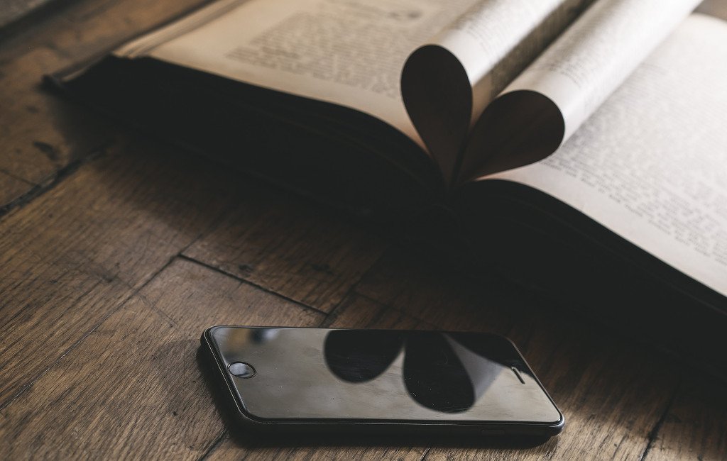 Hojas de un libro forman un corazón que se refleja en un teléfono móvil